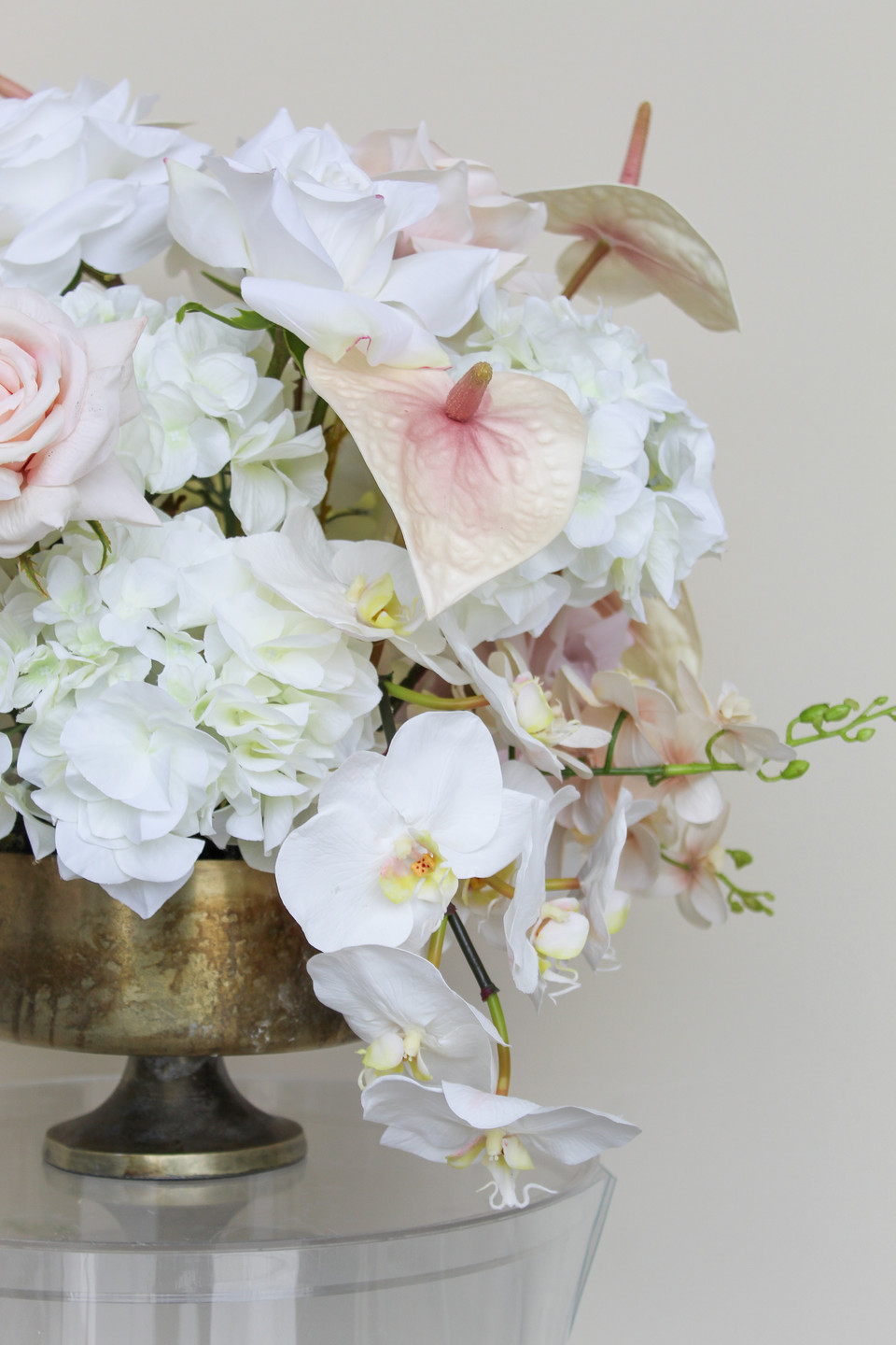 Close-up of a grand centerpiece featuring white hydrangeas, white roses, blush roses, blush anthuriums, and cascading orchids in a gold compote vase.