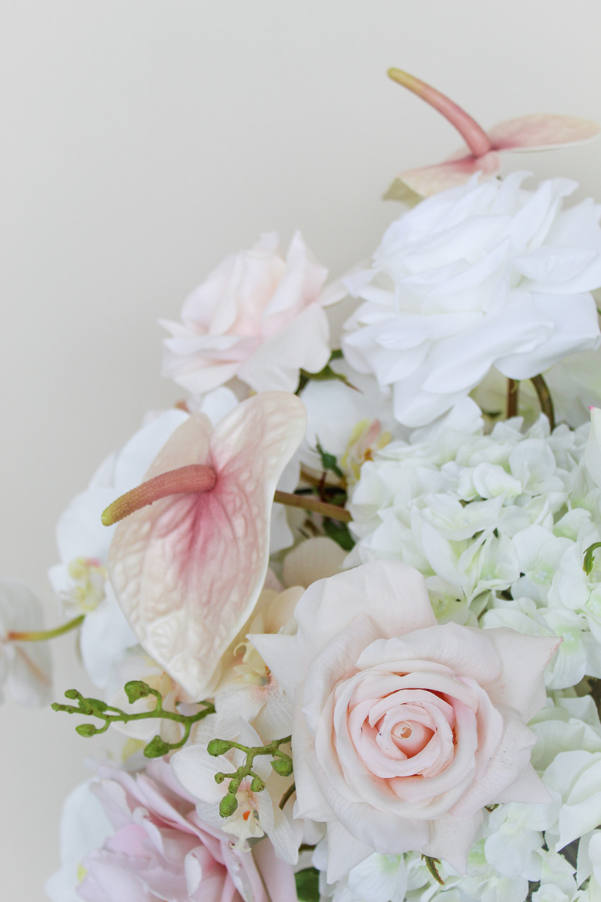 Close-up of a grand centerpiece featuring white hydrangeas, white roses, blush roses, blush anthuriums, and cascading orchids in a gold compote vase.