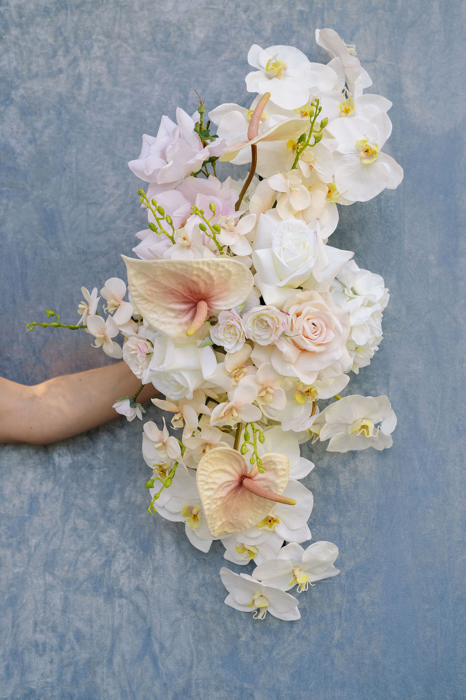 Floral arrangement featuring blush anthuriums, white orchids, ivory roses, hydrangeas, and cascading floral accents.