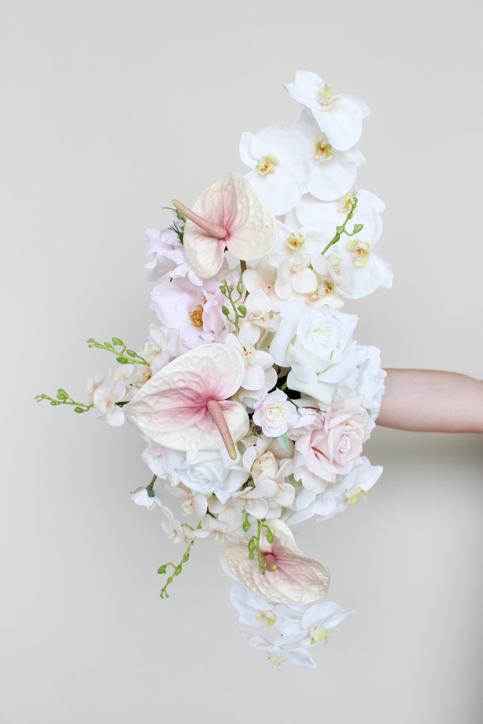 Floral arrangement featuring blush anthuriums, white orchids, ivory roses, hydrangeas, and cascading floral accents.