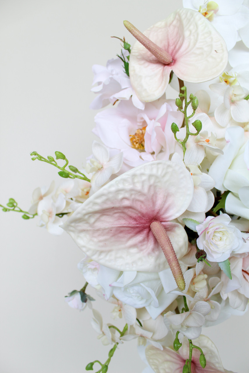 Close-up of a floral arrangement featuring blush anthuriums, white orchids, ivory roses, hydrangeas, and cascading floral accents.
