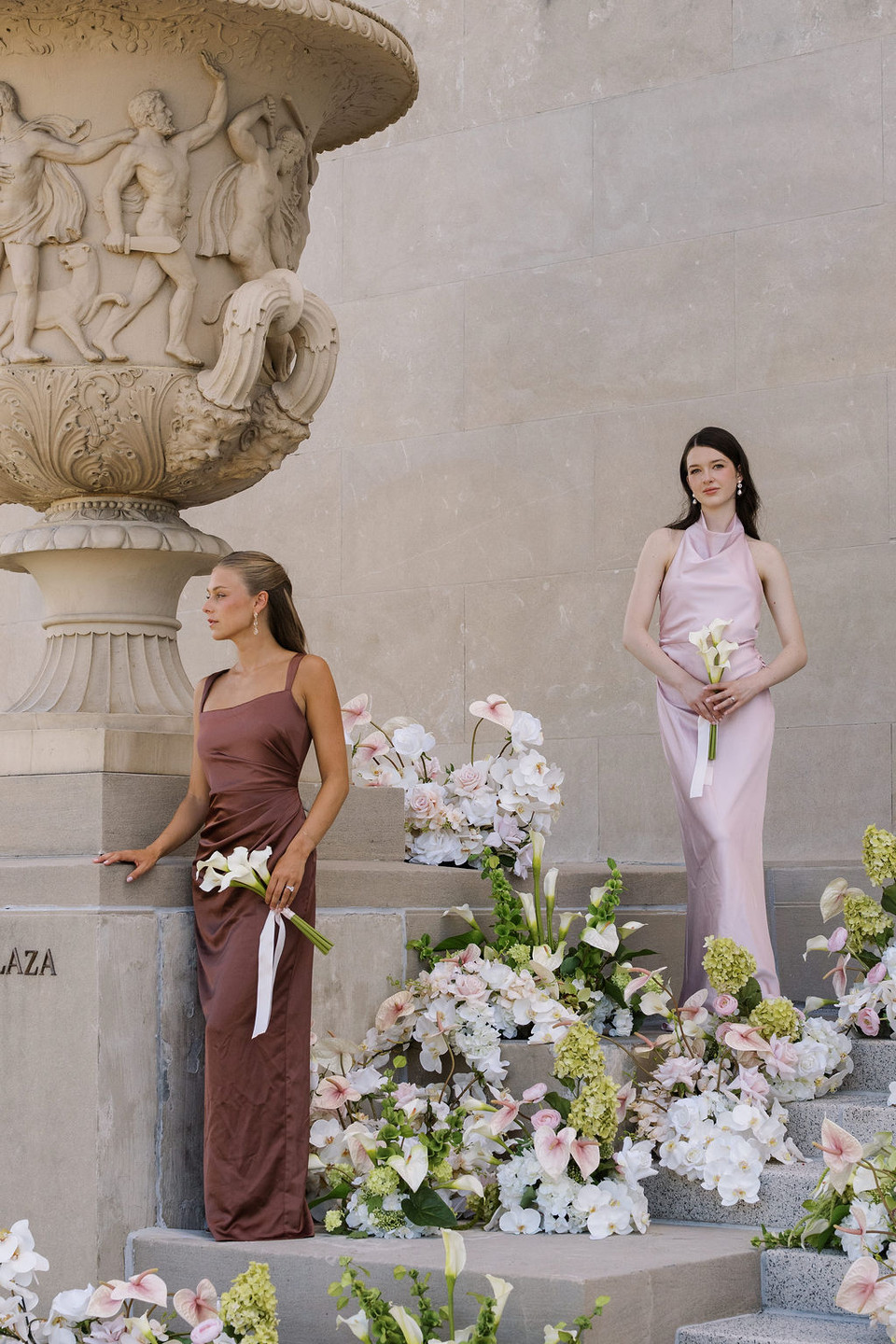 Bridesmaids holding White Calla Lily Petite Bouquets while posing among lush wedding florals in soft blush, white, and green tones on grand stone steps.