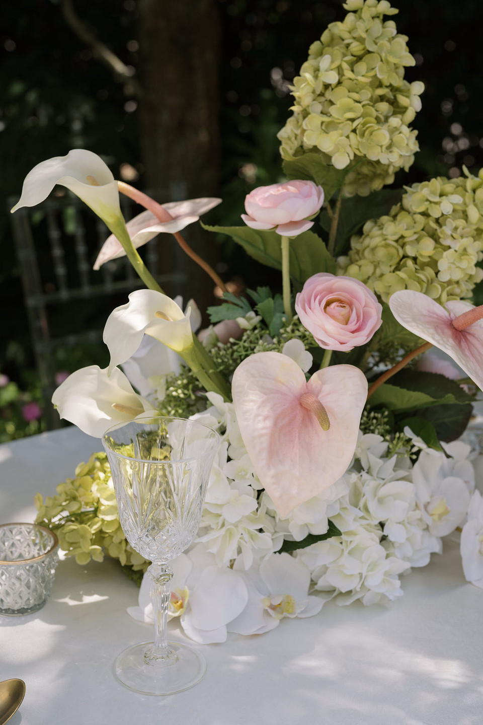 Close-up of a floral arrangement featuring white hydrangeas, blush anthuriums, white orchids, pale pink roses, calla lilies, and soft blush garden roses.