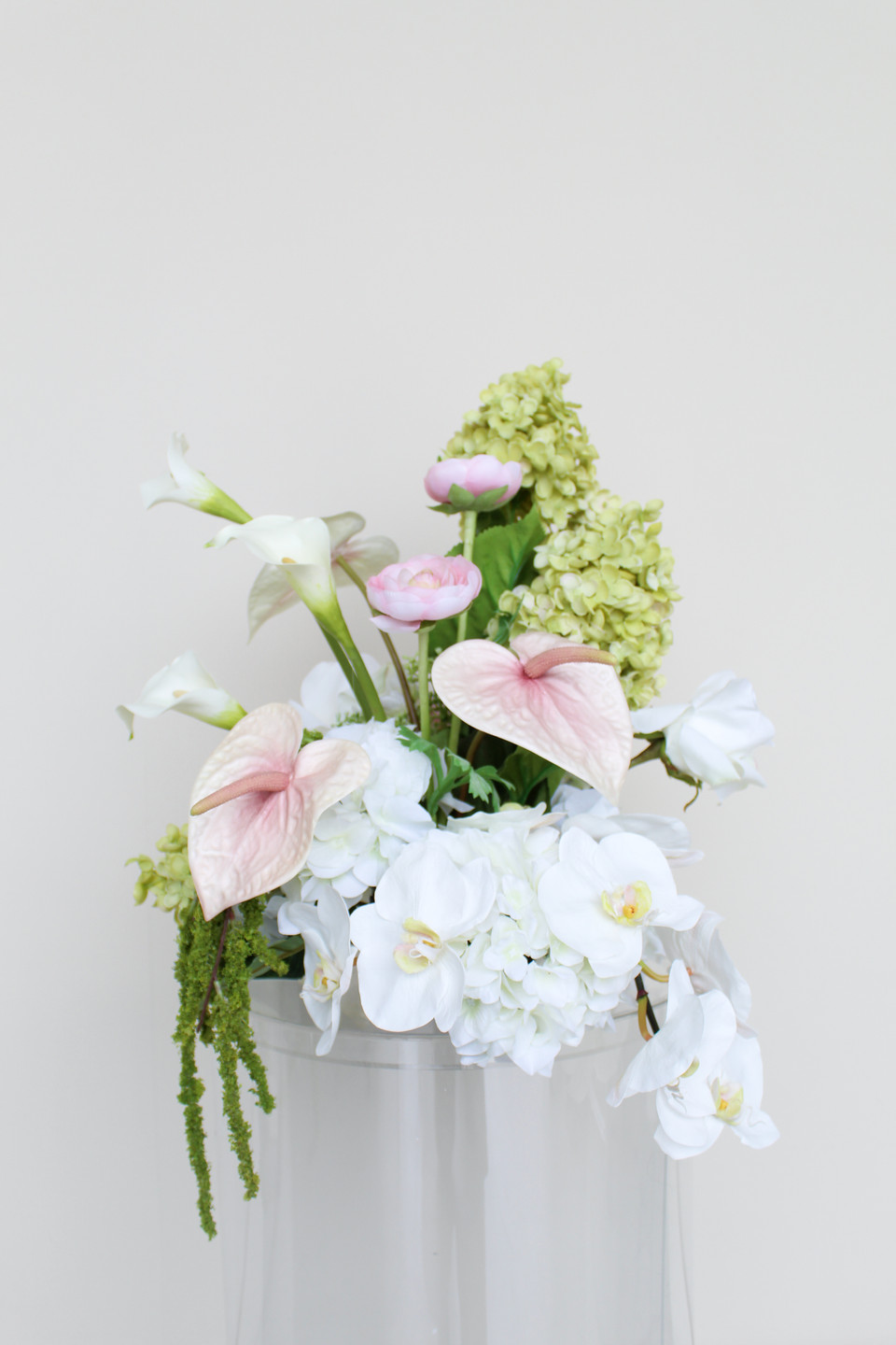 A floral arrangement featuring white hydrangeas, blush anthuriums, white orchids, pale pink roses, calla lilies, and soft blush garden roses.