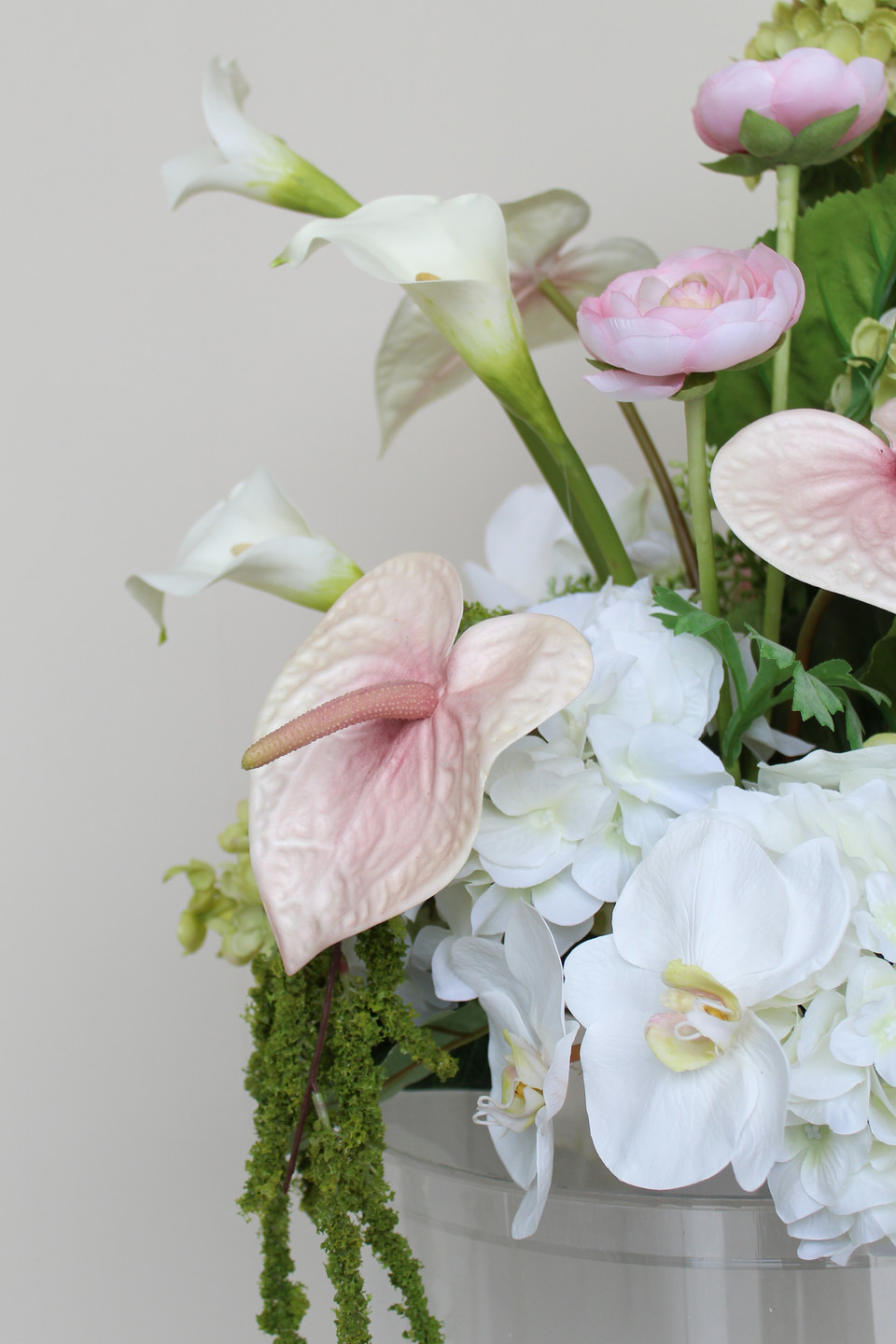 Close-up of a floral arrangement featuring white hydrangeas, blush anthuriums, white orchids, pale pink roses, calla lilies, and soft blush garden roses.