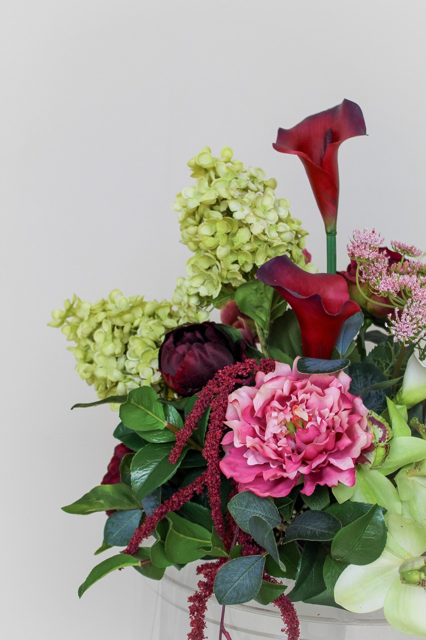 Close-up of the Stella blended large vaseless centerpiece featuring deep burgundy calla lilies, white calla lilies, blush peonies, pale green hydrangeas, green cymbidium orchids, burgundy roses, white anthuriums, cascading burgundy amaranthus, and airy pink accent blooms.