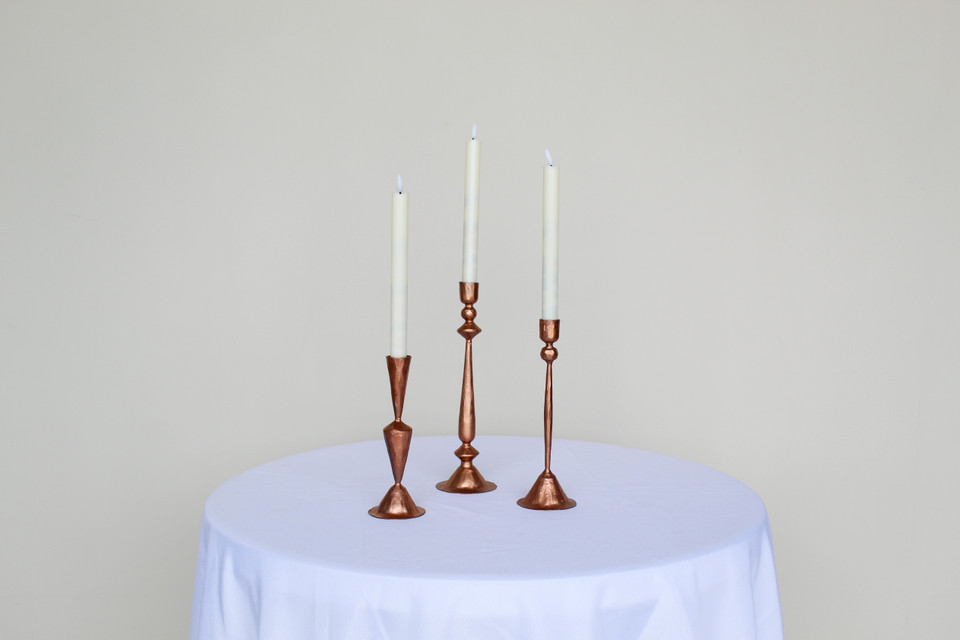 Three copper candlesticks on a white cocktail table in front of a white wall