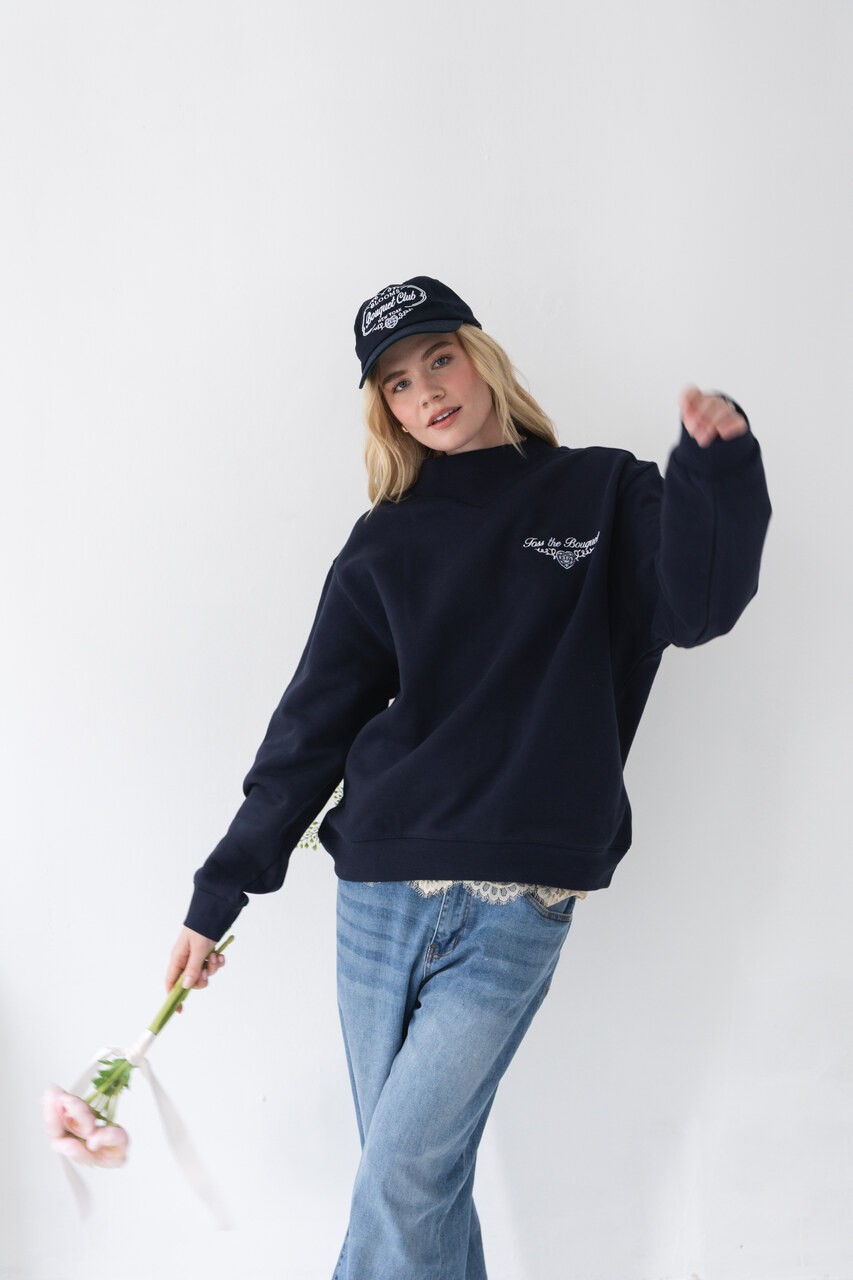 Woman wearing a navy Bouquet Club mockneck sweatshirt styled with light wash jeans.