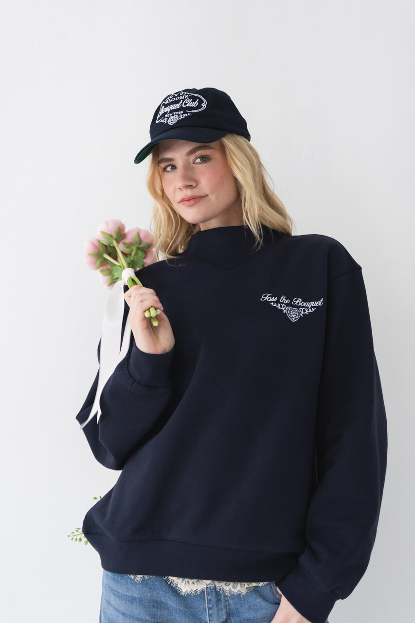 Woman wearing a navy Bouquet Club mockneck sweatshirt with embroidered front logo holding a floral bouquet.