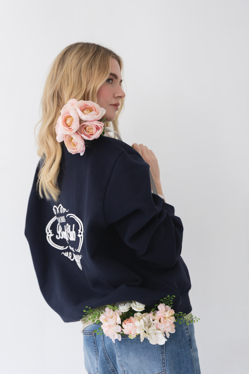 Side profile of a woman wearing a navy Bouquet Club mockneck sweatshirt with embroidered front logo.
