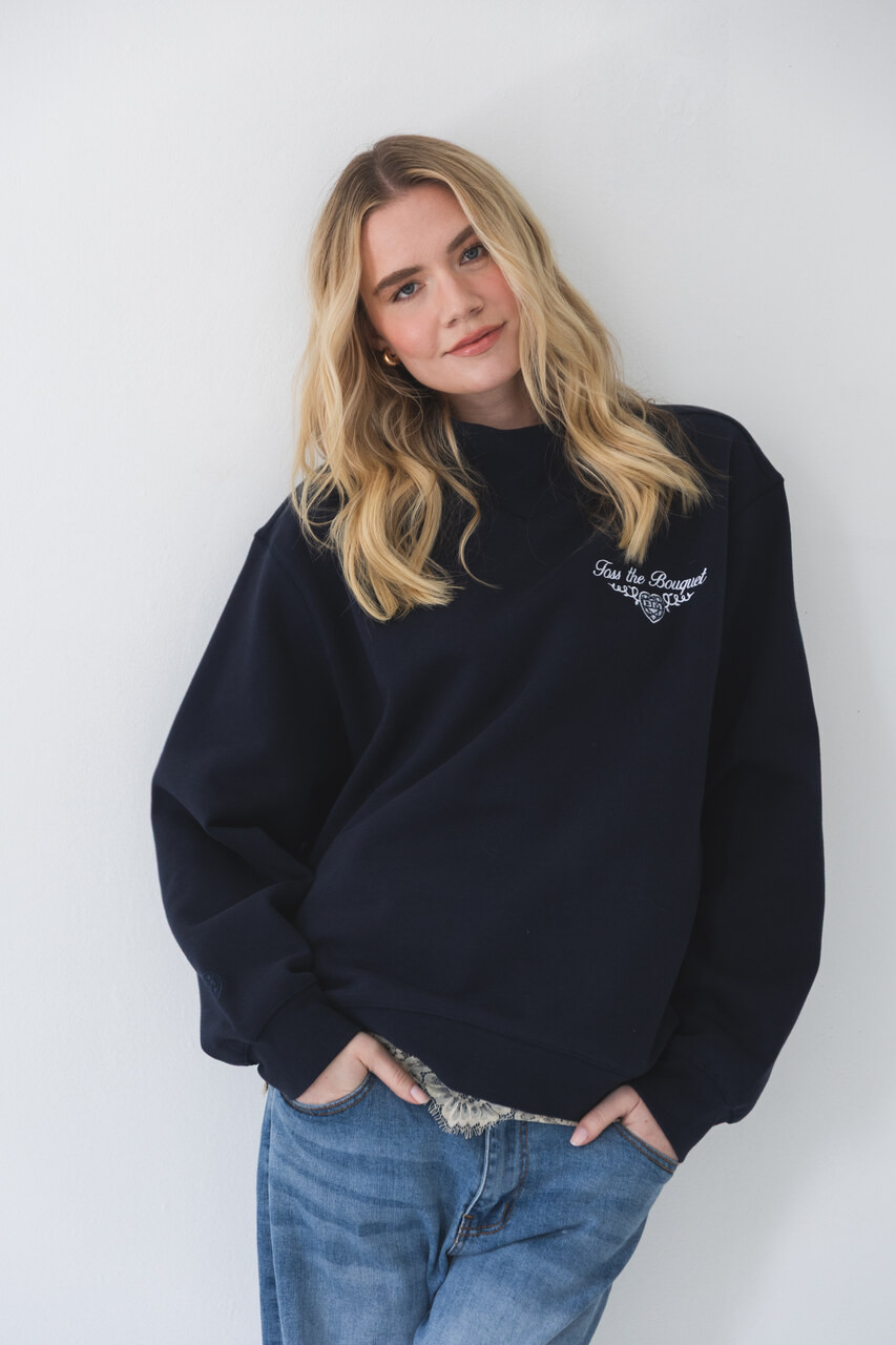 Woman wearing a navy Bouquet Club mockneck sweatshirt with embroidered front logo.