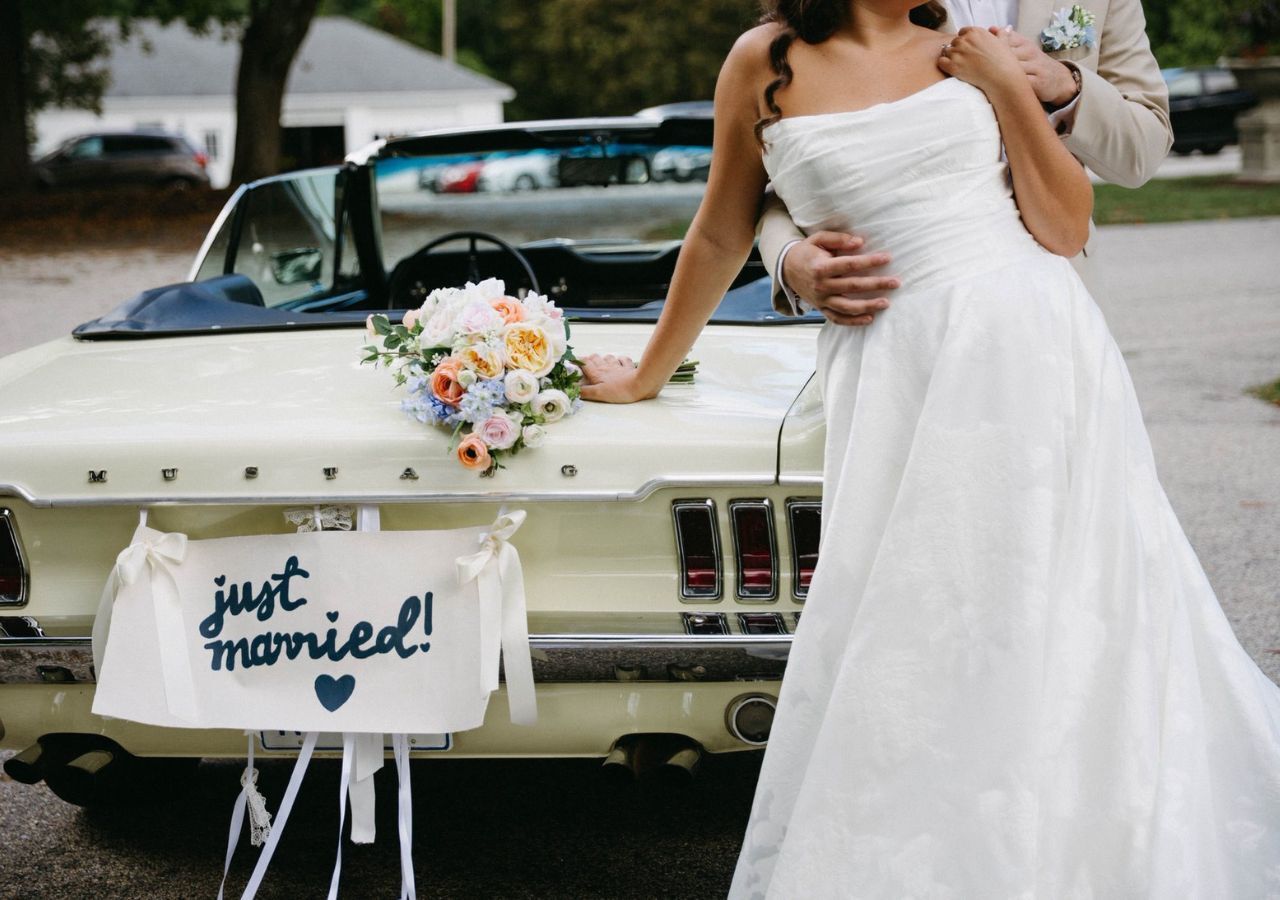 A bride and groom in front of yellow mustang convertible with a'Just Married' sign
