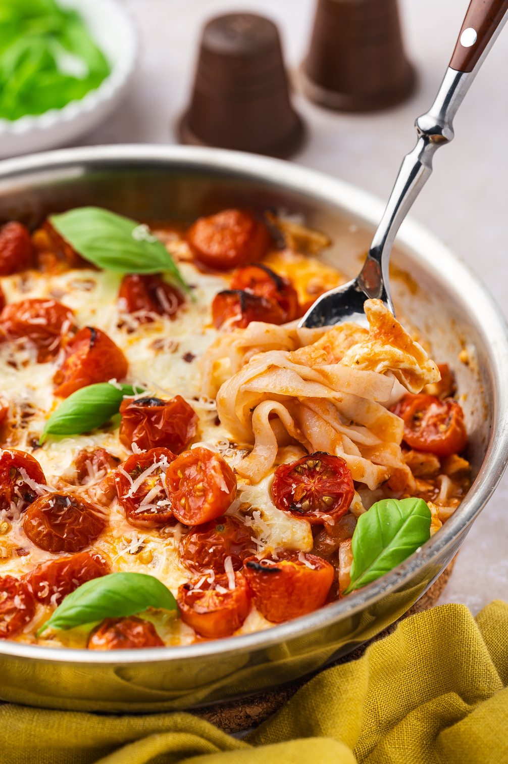 A closeup image of a fork swirling a perfect bite of cheesy Margherita pasta.