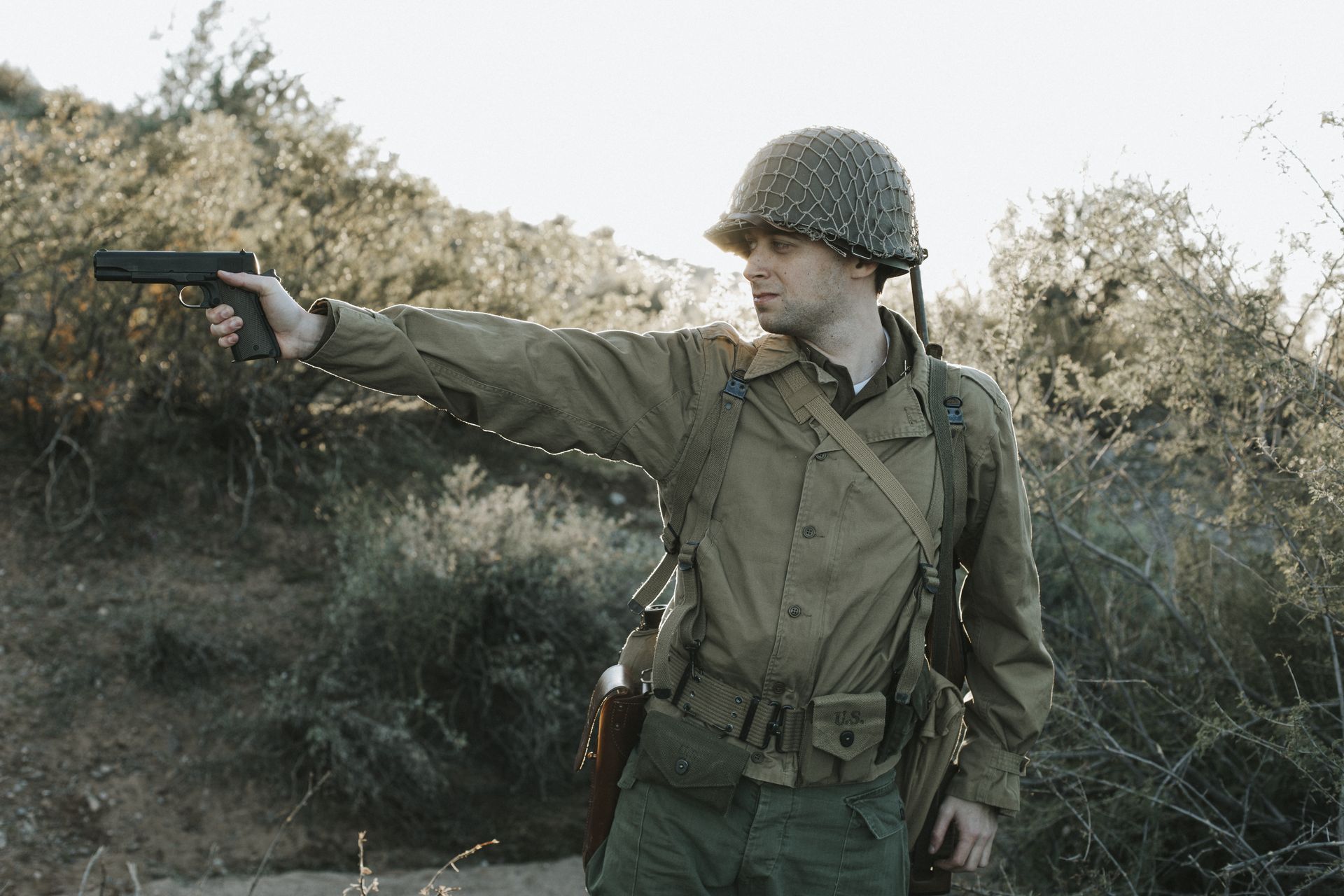 Soldier in WWII pattern uniform aiming a 1911 pistol at golden hour