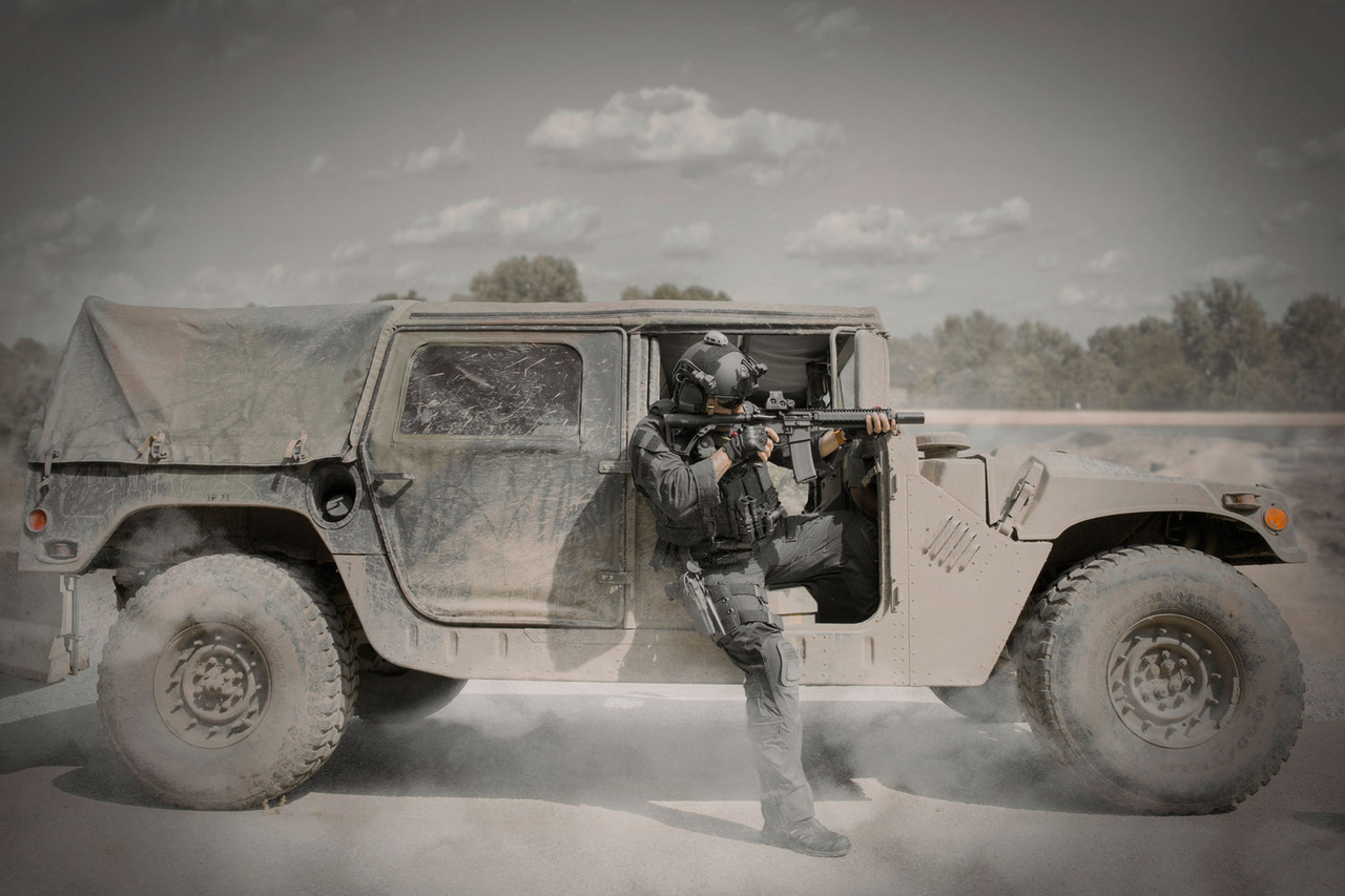 A special operator dress in black  step out of a humvee aiming towards him in the outdoor on sandy field and three line in background horizon.