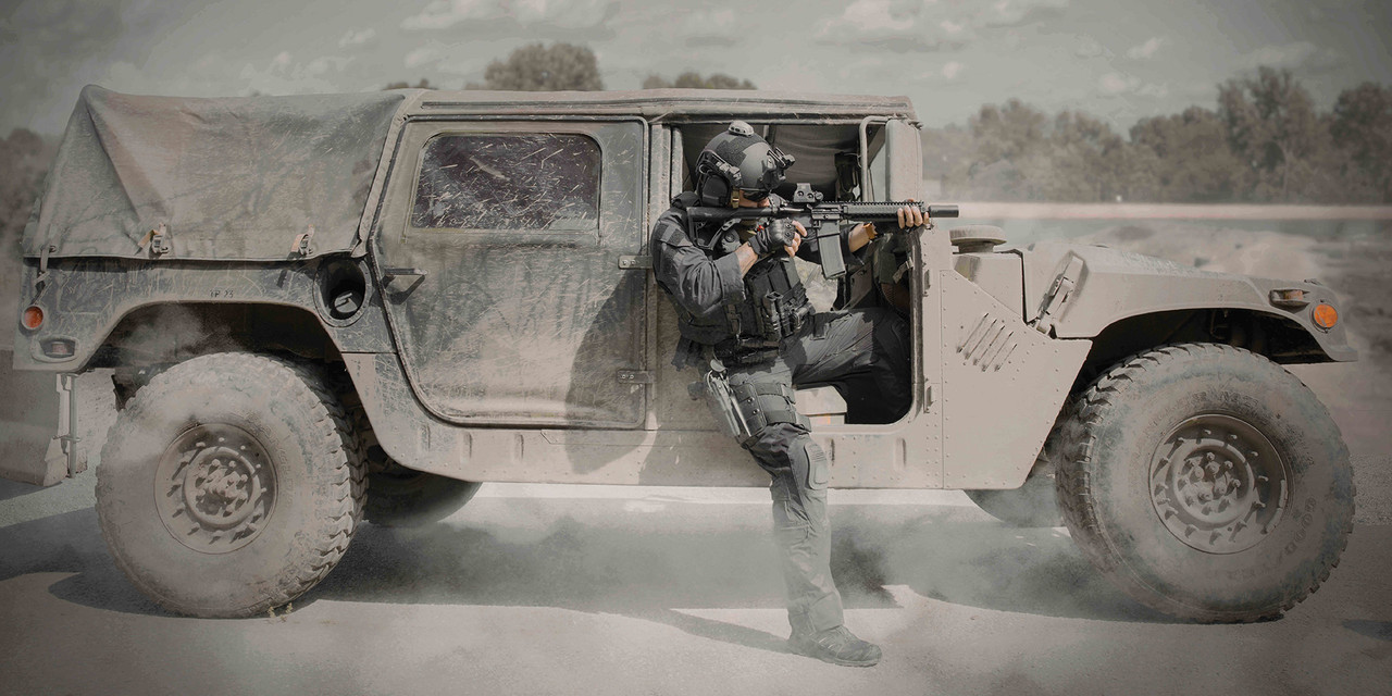 A special operator dress in black  step out of a humvee aiming towards him in the outdoor on sandy field background.