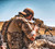 Operator aiming downrange with Carcajou Tactical 3D Ghillie Wrap on a sniper rifle in a desert under a bright blue sky, available from Hudson Supplies Corp.