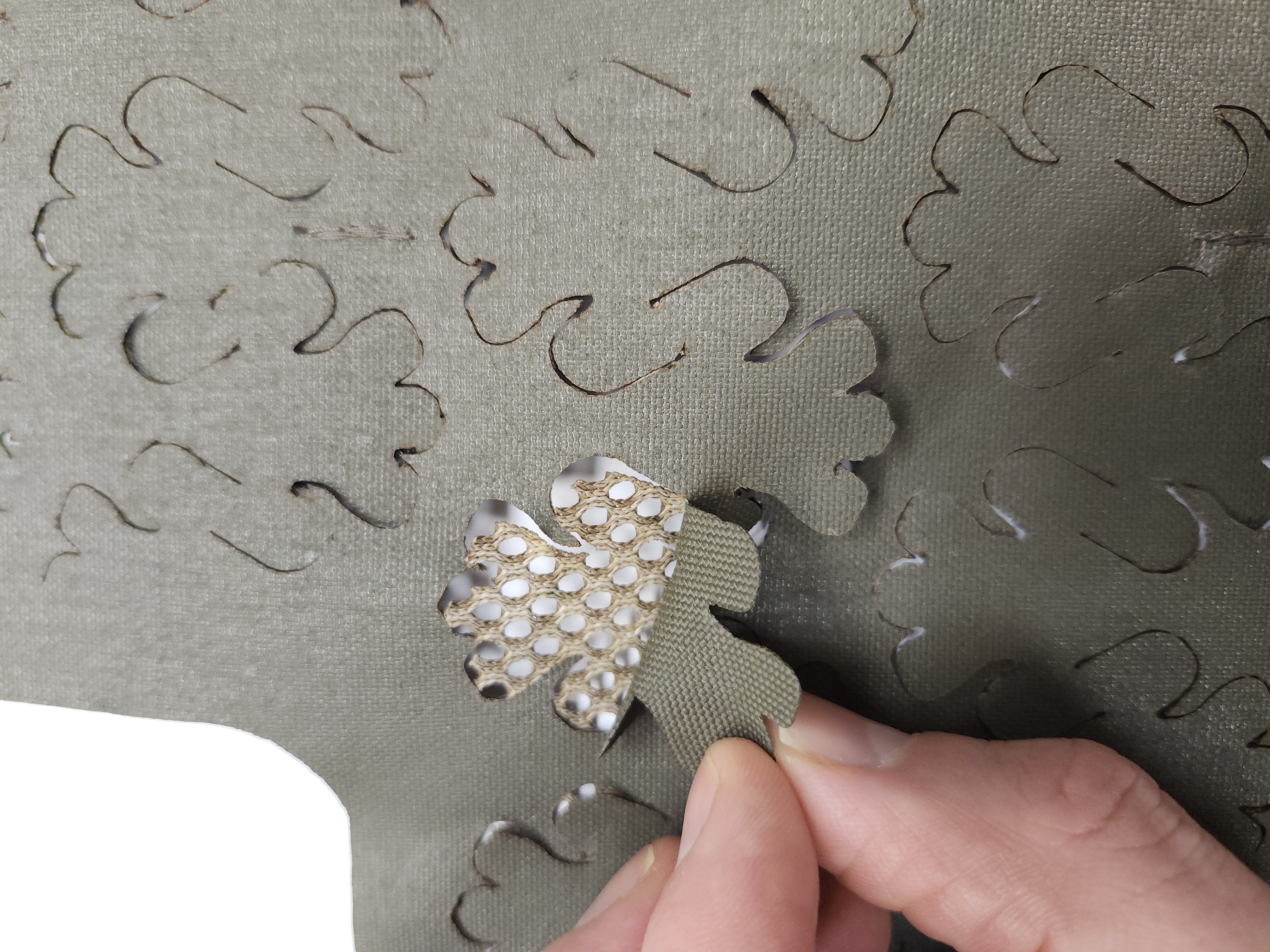 Close-up of Carcajou Tactical helmet scrim in Ranger Green showing laser-cut leaf detail and mesh backing layer