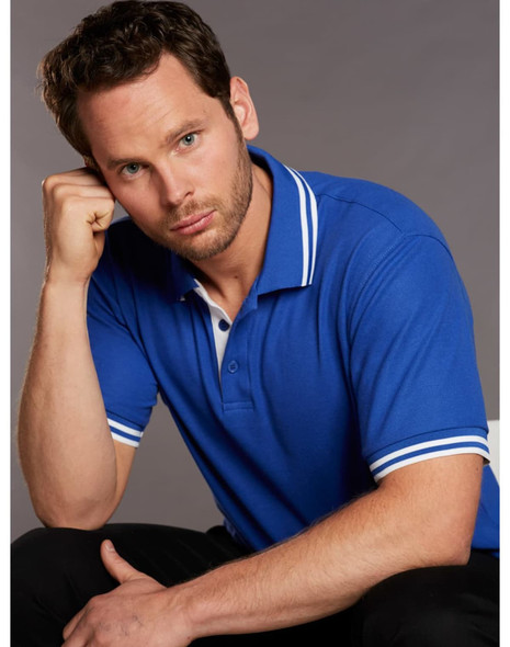 A blue polo shirt featuring white detailing on the collar and sleeves, modelled by a man.