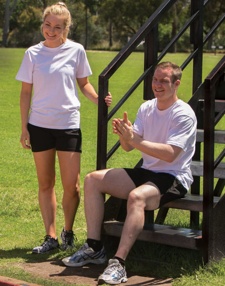 Two individuals wearing white premium t-shirts and black shorts, one sitting on a stair and the other standing nearby.