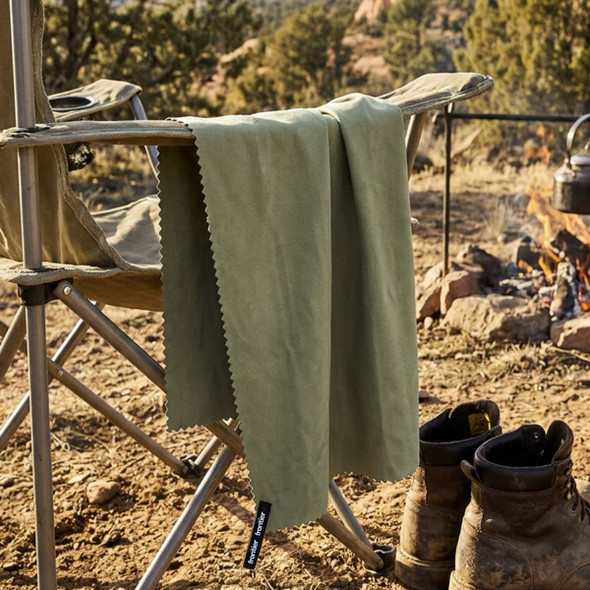 A green Frontier Rapid Dry Towel hangs from a camping chair beside a fire, with boots on the ground nearby.