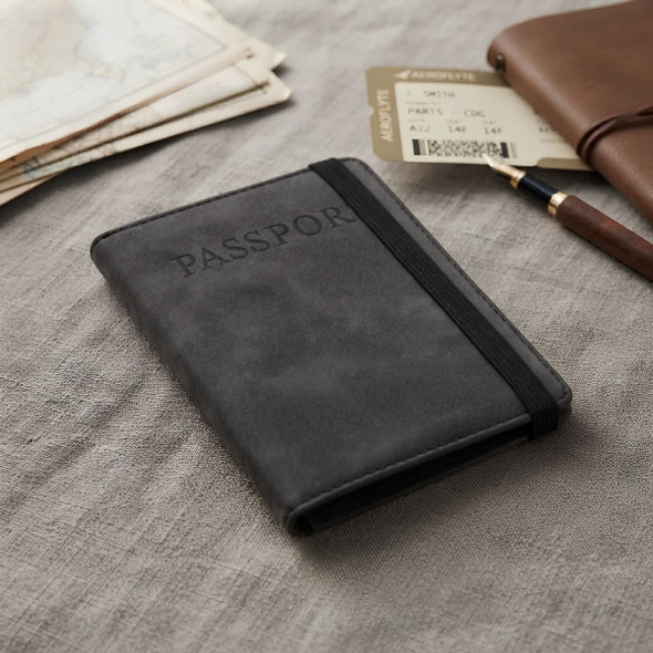 A black passport wallet with an elastic band, resting on a textured surface alongside travel documents and a pen.