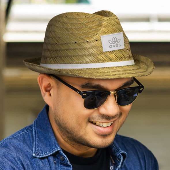 A straw Santiago Fedora hat in natural tones, featuring a logo patch, worn by a smiling person with sunglasses.