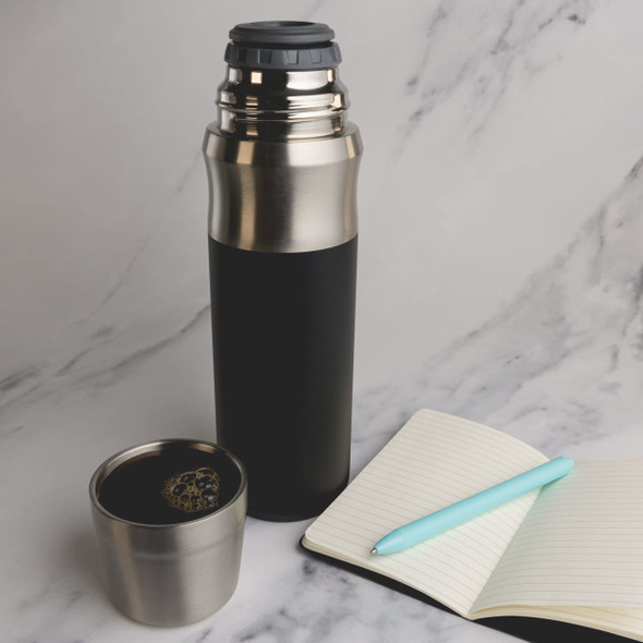 A drink bottle in black and stainless steel, with a matching cup and a notebook on a marble surface.
