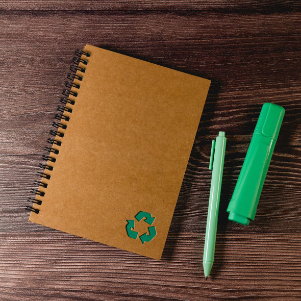 A brown spiral-bound notebook with a recycling symbol, accompanied by a green pen and a green highlighter.