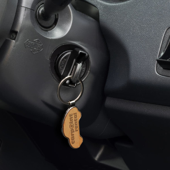 A car-shaped wooden key ring with a metal keychain, inserted into a car ignition.