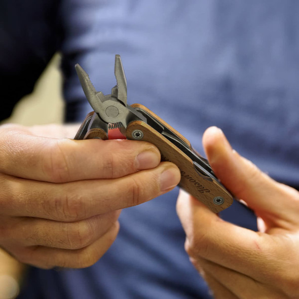 A wooden multi-tool with pliers in a person's hand, featuring various tools and a logo on the handle.