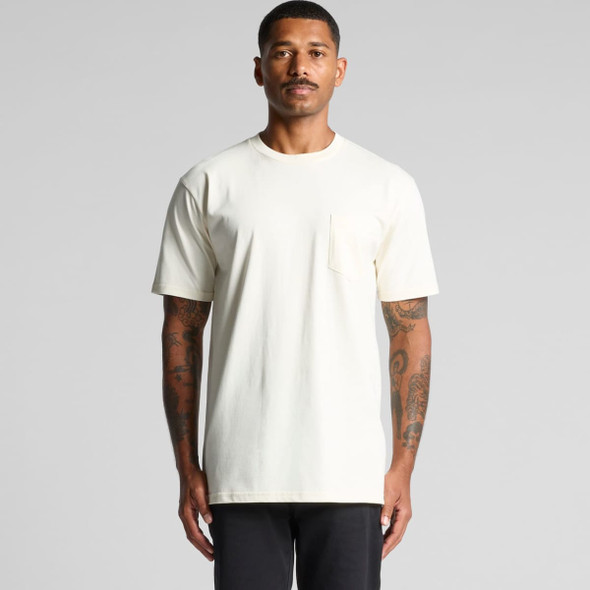 A light cream-coloured T-shirt with a pocket and a crew neck, worn by a man. The shirt has a logo.
