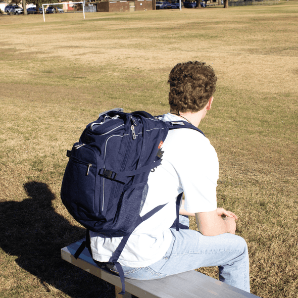 A navy blue High Sierra Access 3.0 Backpack 45L worn on the back of a person sitting on a bench.