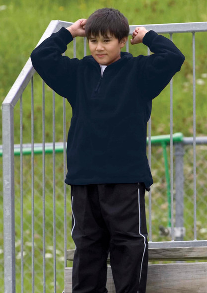 A boy wearing a black detailed polar fleece pullover stands on a metal structure, with green grass in the background.