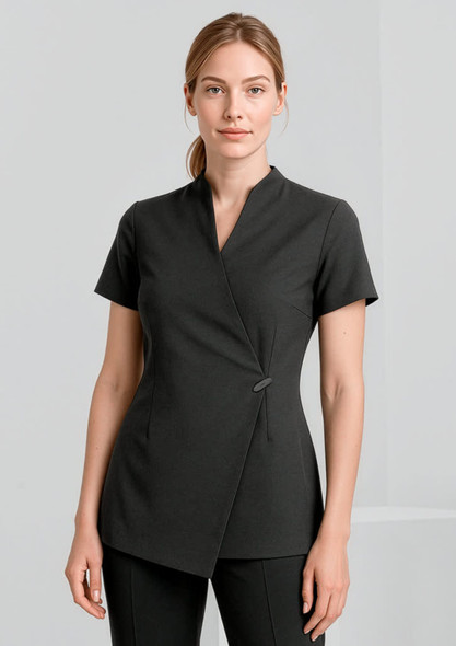 A woman is wearing a black spa tunic with a wrap design and short sleeves. The tunic features a simple button detail.