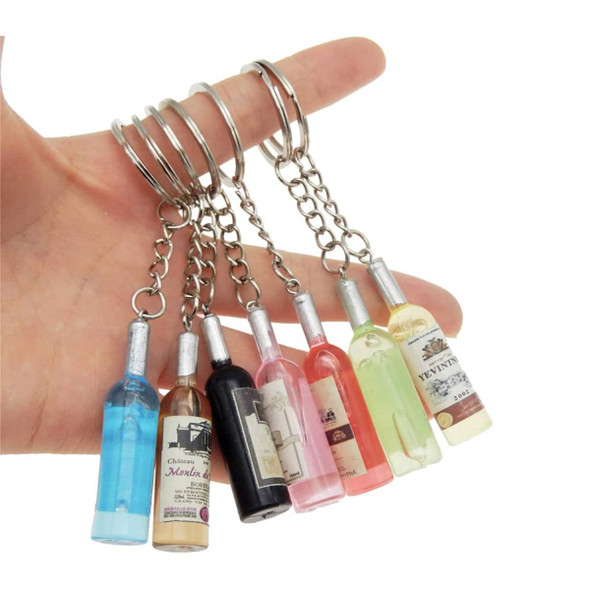 A hand holding multiple custom-shaped resin keychains in various colours resembling miniature bottles.