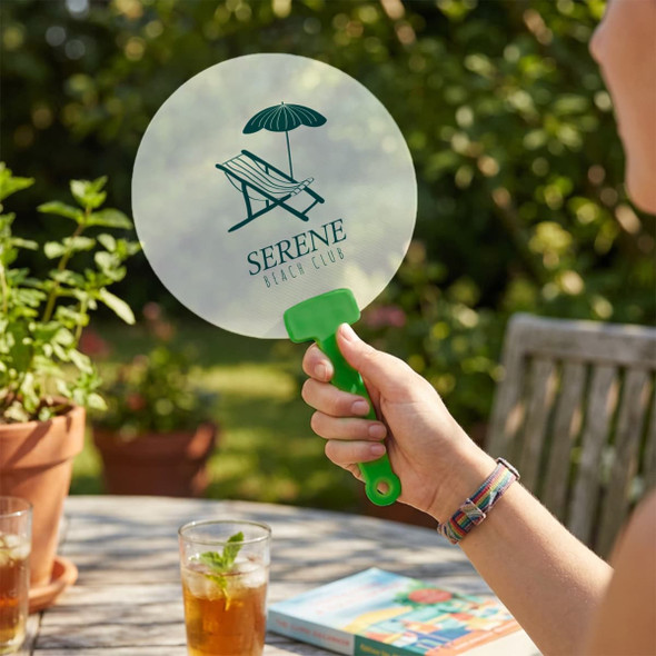 A circular, transparent fan with a green handle, featuring a logo of a sun umbrella and deck chair.