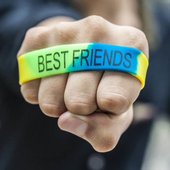 A vibrant silicone wristband in yellow, green, and blue, featuring "BEST FRIENDS" text. The design includes a logo.