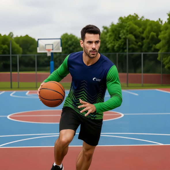 A man in a blue and green long-sleeve shirt dribbles a basketball on a court with a hoop in the background.