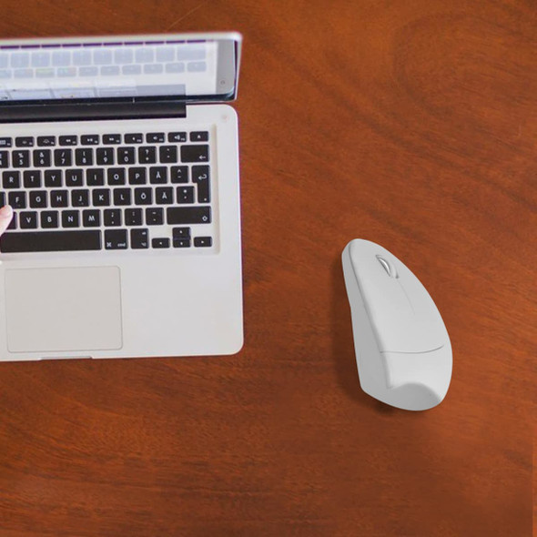 An ergonomic white wireless mouse next to a silver laptop on a wooden desk.