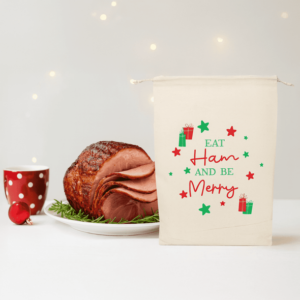 A cream-coloured bag with festive designs next to a glazed ham on a platter and a red polka dot cup.