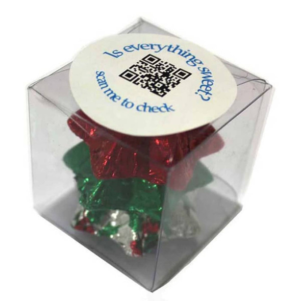 A clear cube containing Christmas-themed chocolates in red, green, and silver foil, with a circular label on top. A clear cube containing Christmas-themed chocolates in red, green, and silver foil, with a circular label on top.