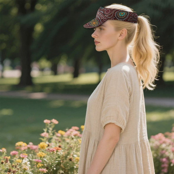 A woman in a beige dress wearing a patterned brown visor stands in a garden with flowers. The visor features a logo. A woman in a beige dress wearing a patterned brown visor stands in a garden with flowers. The visor features a logo.
