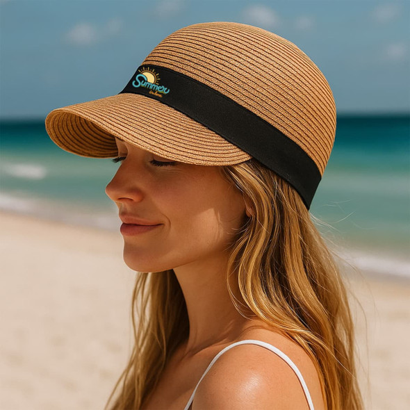 A straw sun hat in light brown with a black band, featuring a logo, situated on a beach background. A straw sun hat in light brown with a black band, featuring a logo, situated on a beach background.