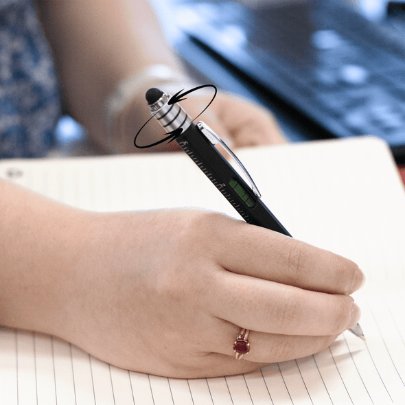 A black and silver pen with a unique balance design is held above a notebook with blank pages.