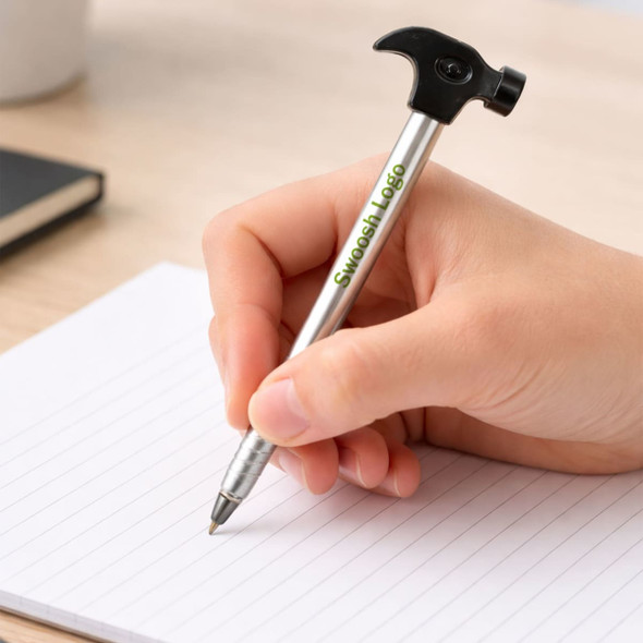 A hammer-shaped ballpoint pen in silver and black, held over a blank notepad with lines.