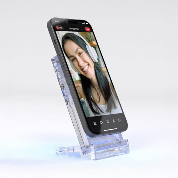 A clear acrylic wireless charging stand displaying a smartphone in a vertical position, featuring a smiling face on the screen.