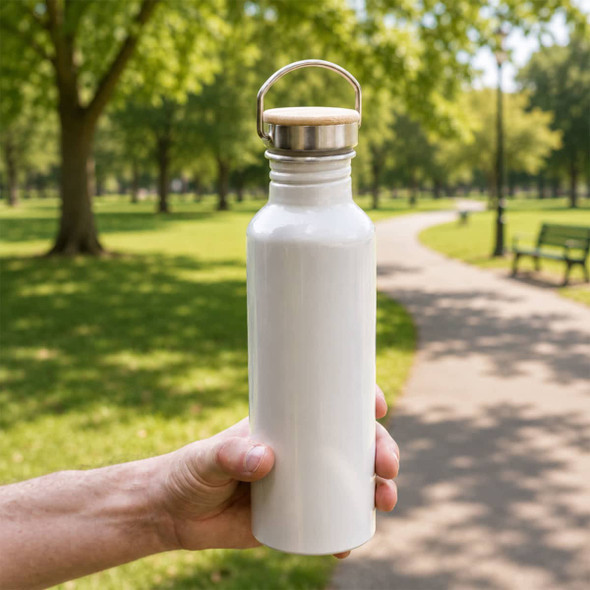 A drink bottle made of recycled aluminium, featuring a silver cap and a smooth white finish, held in a hand outdoors.