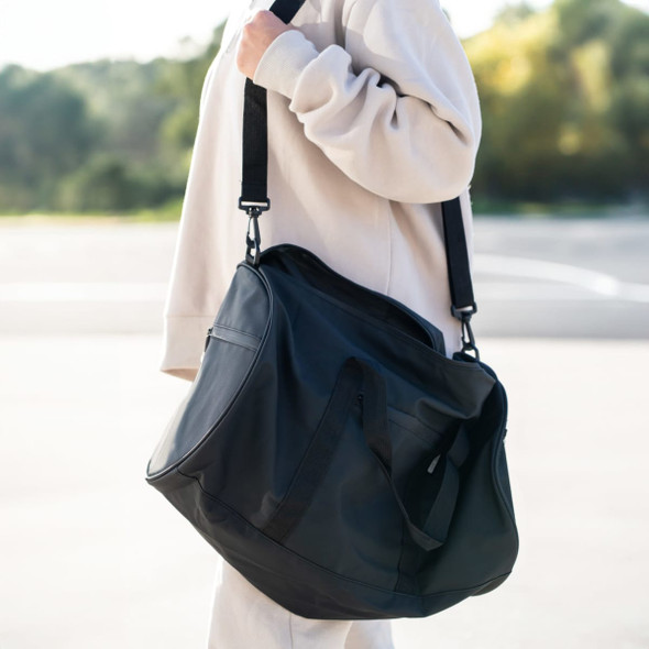 A large black duffle bag with a shoulder strap, carried by a person in a casual outfit against a natural background.