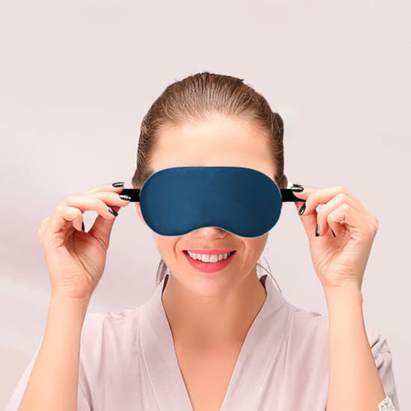 A satin sleep mask in navy blue, being held up by a smiling woman in a light-coloured robe.